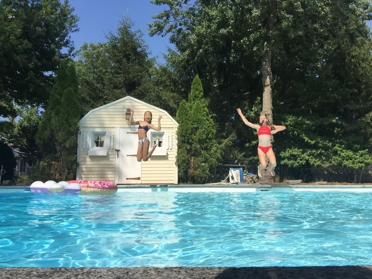 Kids having fun jumping into the backyard pool on a sunny day